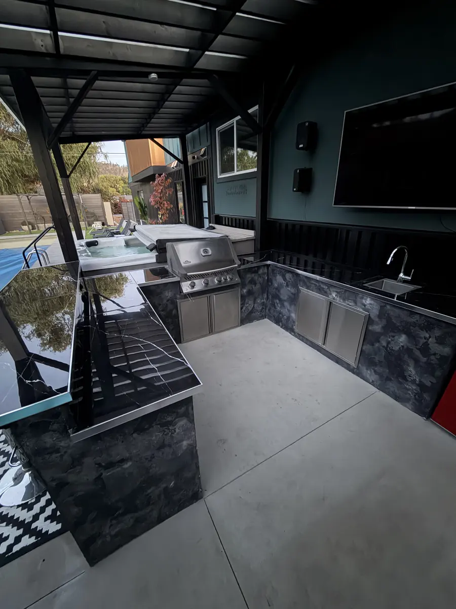 The new covered custom outdoor kitchen with grill, sink and black counters
